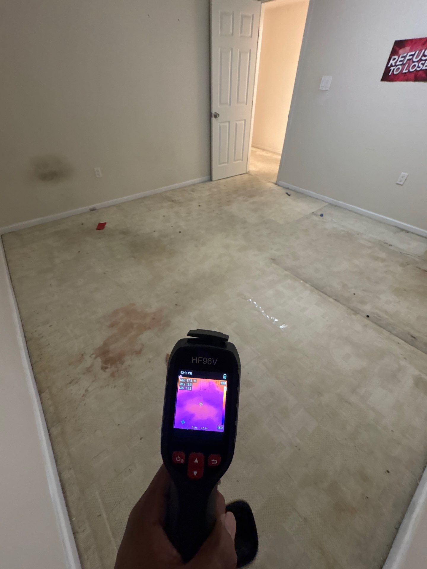 Technician mapping moisture patterns across wall and floor surfaces during restoration inspection.