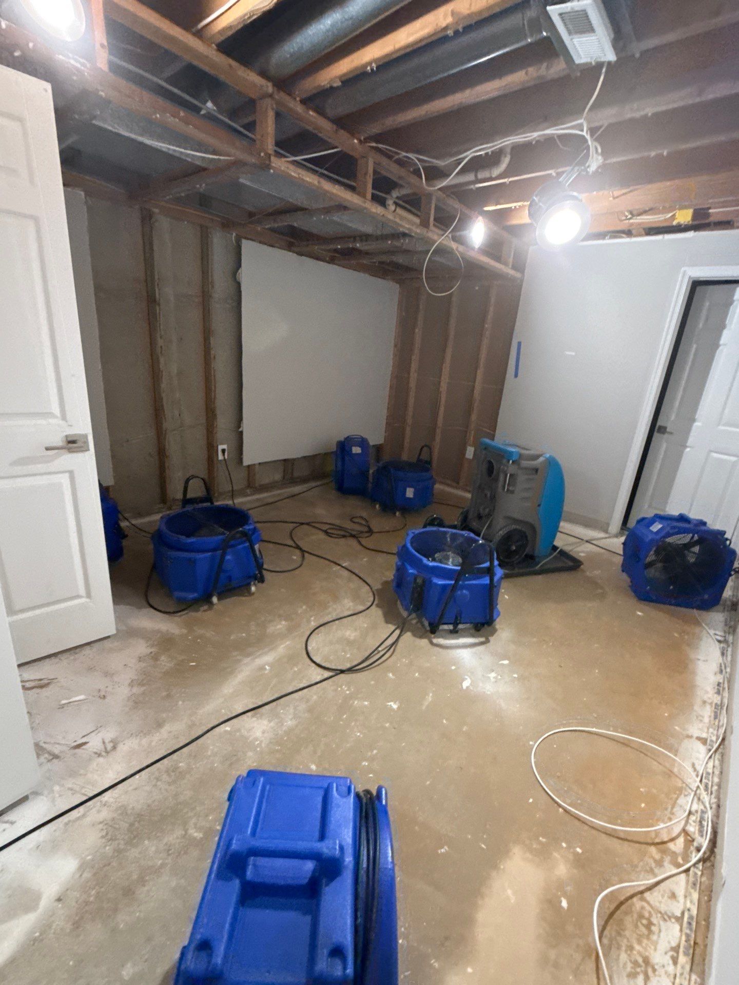 Mid-stage water restoration showing dehumidifiers and air movers deployed for structural drying in Fairfax home.