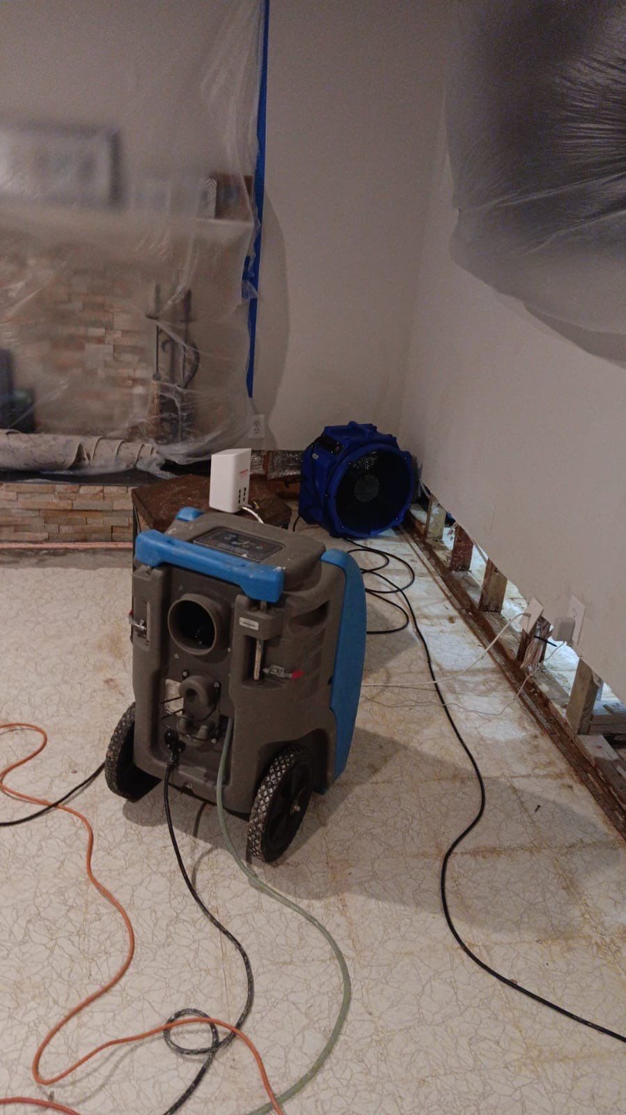 Drying equipment operating during mid-stage water restoration, monitoring moisture levels in building materials.