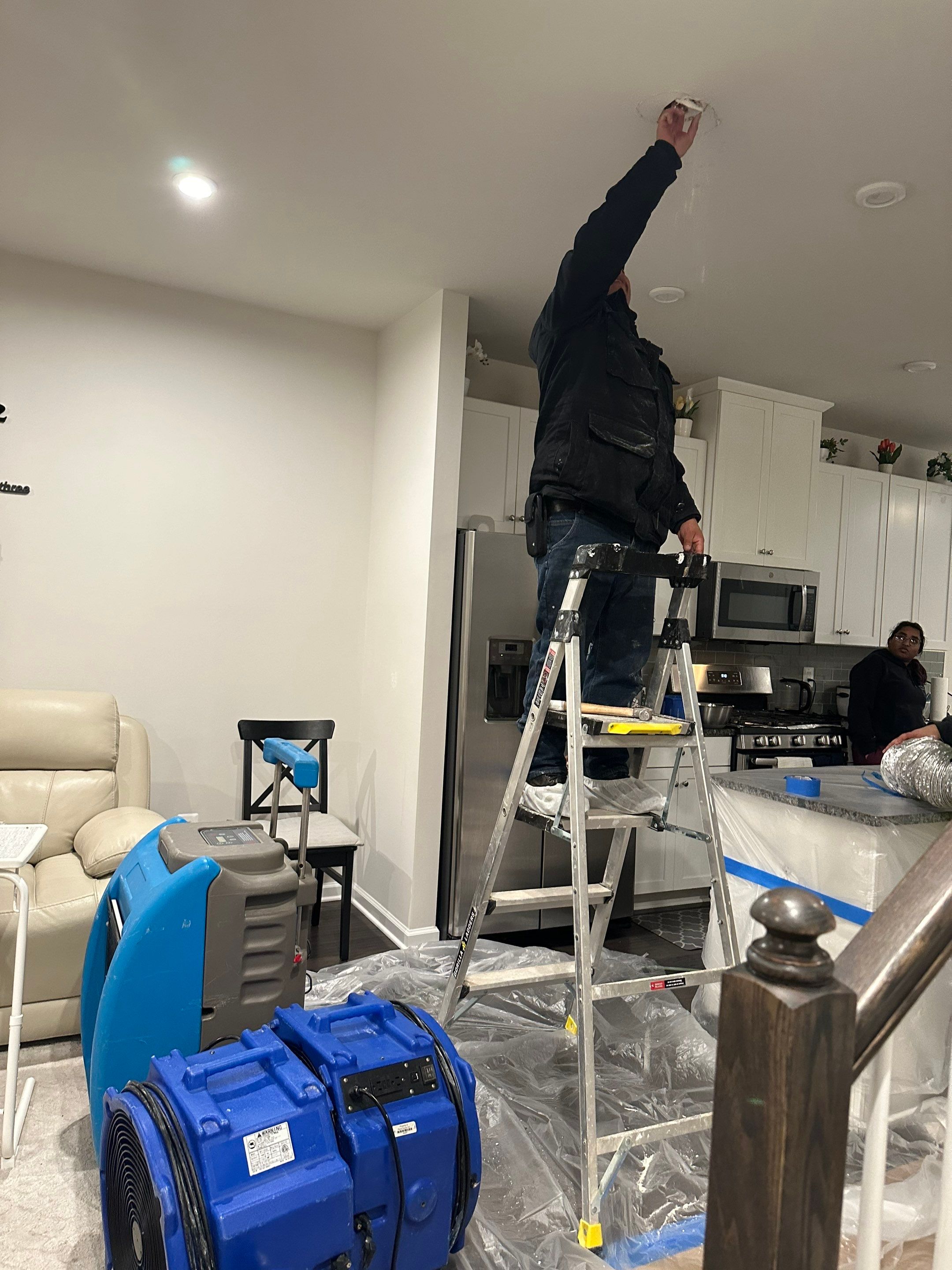 Mid-stage water damage restoration showing active dehumidification and barrier containment.