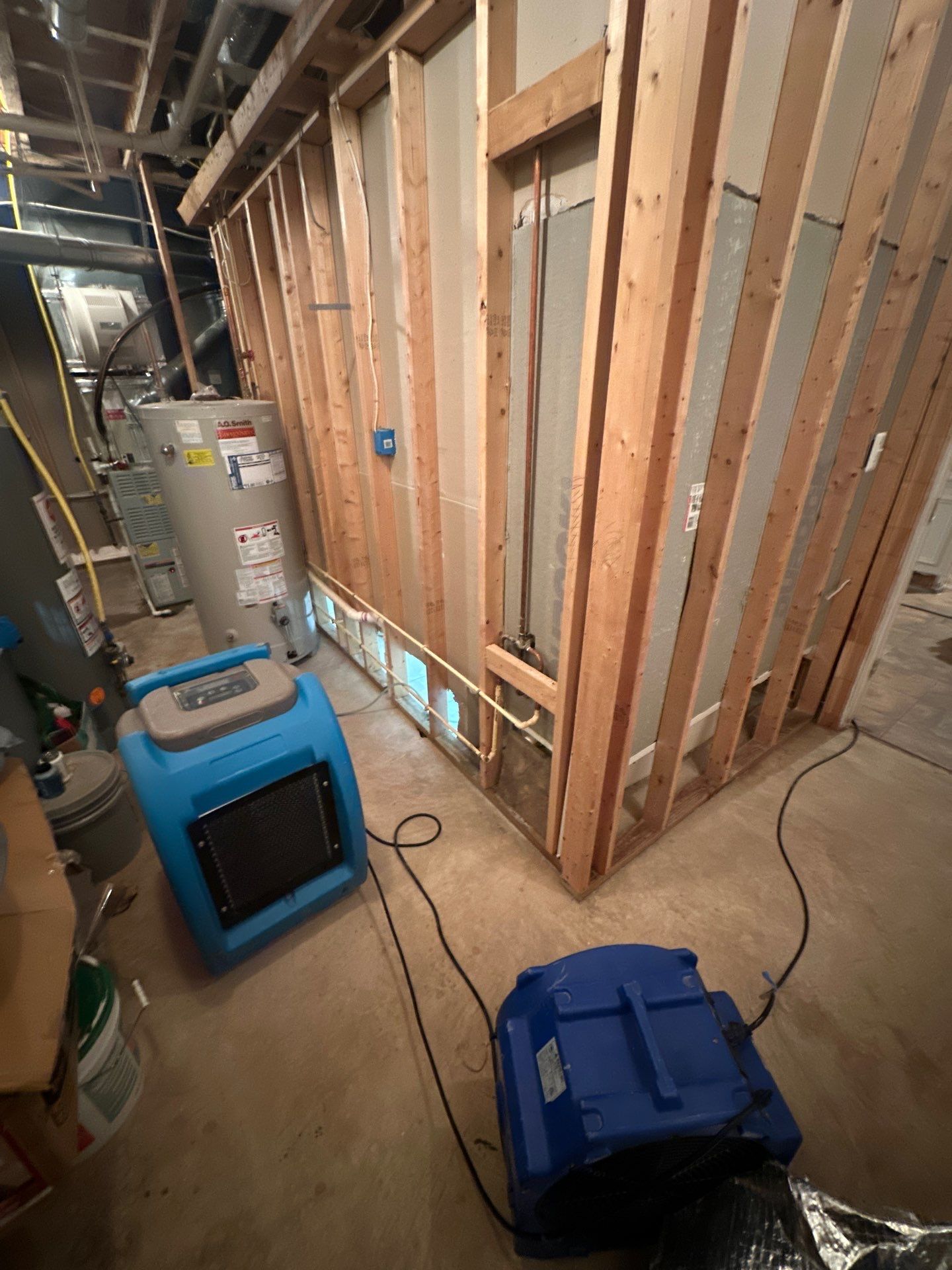 Structural drying underway with dehumidifiers and air movers positioned to manage moisture in walls and subfloor.