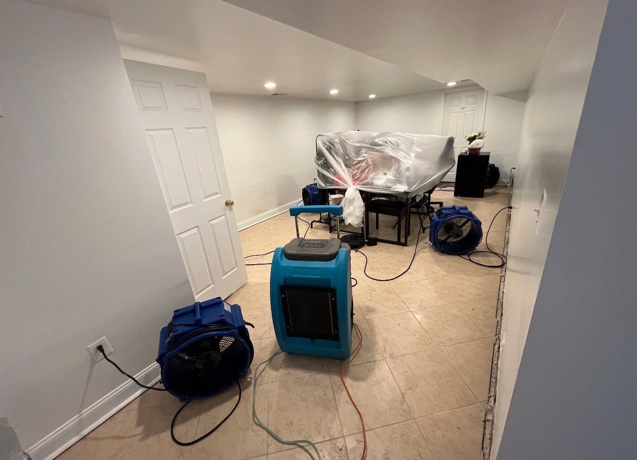 Standing water extraction underway in Falls Church water damage restoration, dehumidifier positioned for structural drying.